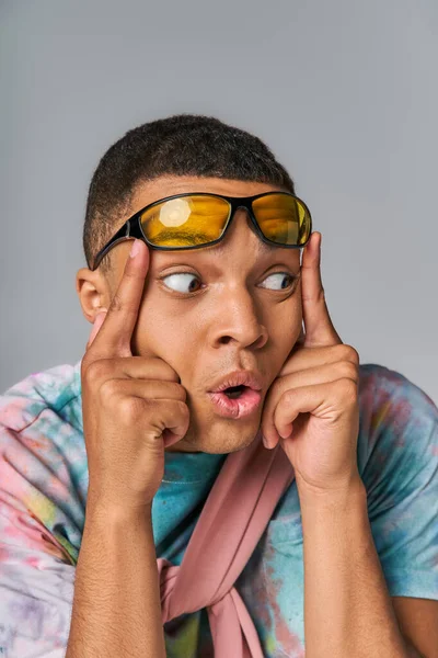 Uomo afroamericano sorpreso con occhiali da sole alla moda guardando altrove sul grigio — Foto stock
