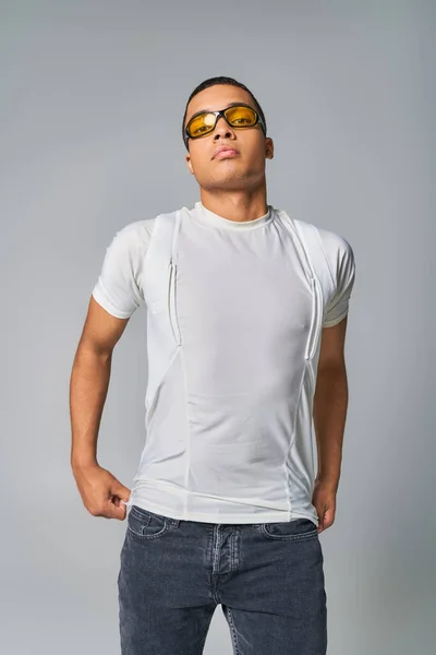 Moda moderna, cara americano africano em t-shirt, jeans e óculos de sol olhando para a câmera em cinza — Fotografia de Stock