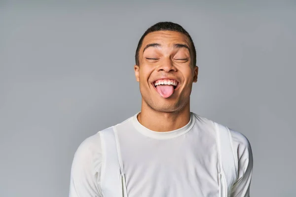 Funny african american man in trendy t-shirt, with closed eyes, sticking out on grey background — Stock Photo