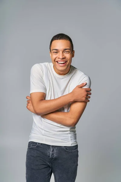 Aufgeregter Afroamerikaner im stylischen T-Shirt blickt in die Kamera und lacht auf grau — Stockfoto