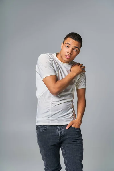 Selbstbewusster Afroamerikaner in T-Shirt und Jeans, mit der Hand in der Tasche, Blick in die Kamera auf grau — Stockfoto