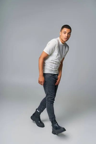 Moderno afroamericano en camiseta y jeans, mirando a la cámara en gris, tendencia de la moda - foto de stock