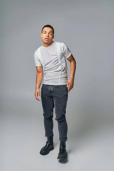 Mode jeune, afro-américaine tendance en t-shirt et jeans, regardant caméra sur gris — Photo de stock