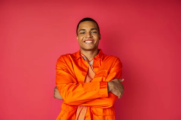 Heureux homme afro-américain en chemise orange, avec les mains pliées, regardant la caméra sur rouge — Photo de stock