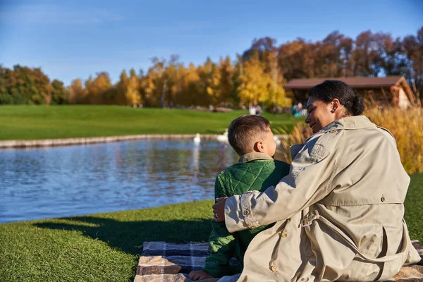 Herbstliches Picknick, Bindung zwischen Mutter und Kind, Afroamerikanerin umarmt Jungen, Teich, Schwäne — Stockfoto