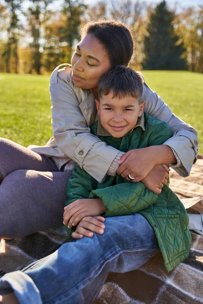 Vínculo y amor, madre abrazando hijo, mujer afroamericana feliz y niño en ropa de abrigo, temporada de otoño - foto de stock