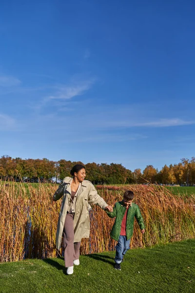 Bindung, Mensch und Natur, glückliche afrikanisch-amerikanische Mutter läuft mit Sohn, Oberbekleidung, Herbst — Stockfoto