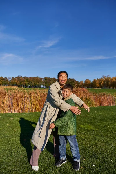 Legame, natura autunnale, felice madre afro-americana che abbraccia il figlio, famiglia in capispalla, autunno — Foto stock