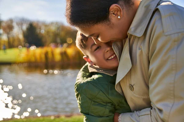 Candid, autumn season, happy african american woman in outerwear hugging cheerful son, portrait — Stock Photo