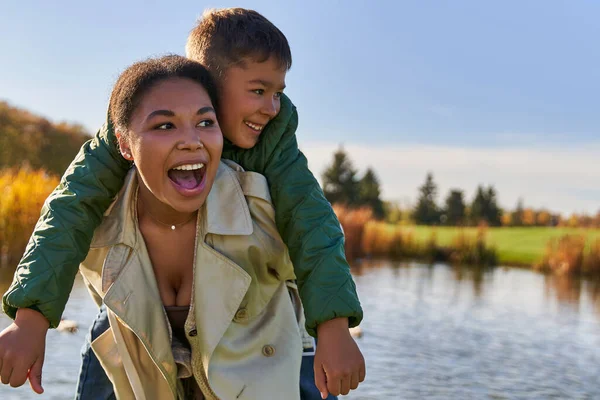 Excited mother piggybacking son, african american woman and boy, childhood, autumnal season — Stock Photo