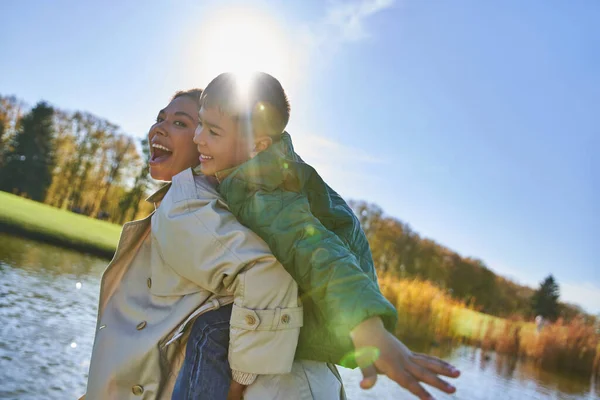 Candid, free spirit, excited mother piggybacking son, african american woman and boy, autumn — Stock Photo