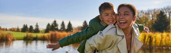 Joyful mother piggybacking son, african american woman and boy, autumn season, free spirit, banner — Stock Photo