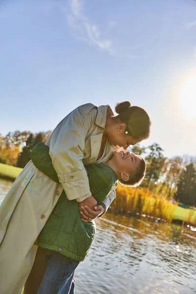 Сімейний зв'язок, любов, щаслива афроамериканська мати і дитина обіймаються біля озера, природа, осінь, посмішка — стокове фото