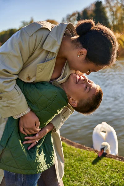 Family bond, love, happy african american mother and child hugging near lake, nature, autumn, fun — Stock Photo