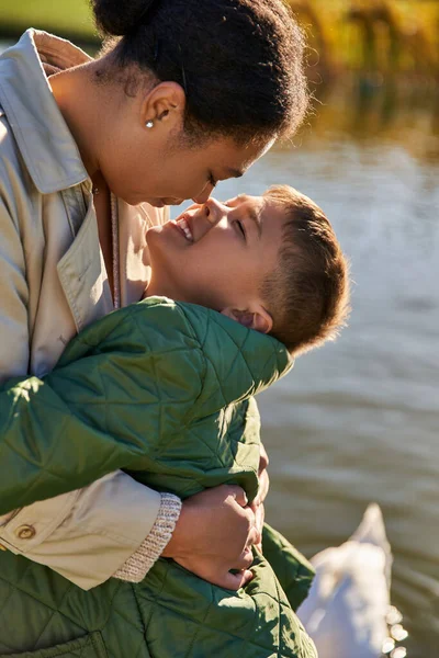 Amore materno, felice ragazzo che abbraccia la madre vicino al lago, famiglia afro-americana, stagione autunnale, autunno — Foto stock