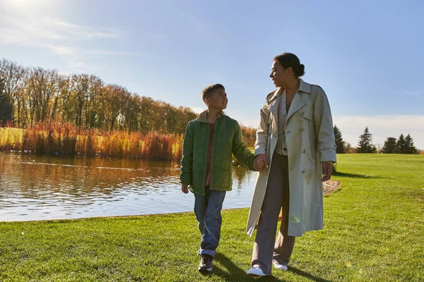 Alegria, mãe e filho de mãos dadas e caminhando perto do lago no parque, família afro-americana, tranquilo — Fotografia de Stock