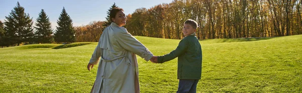 Journée ensoleillée, femme afro-américaine marchant avec son fils dans le parc, herbe verte, tenues d'automne, bannière — Photo de stock