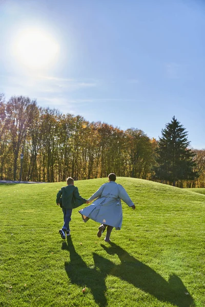 Giornata di sole in autunno, donna afroamericana che corre insieme al figlio nel parco, candida, giocosa — Foto stock