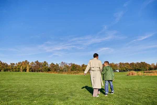Madre e figlio, donna afro-americana che cammina insieme al ragazzo nel parco, candida, giornata di sole, autunno — Foto stock