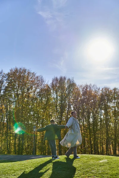 Madre e hijo alegre, mujer afroamericana caminando junto con el niño en el parque, día soleado, otoño - foto de stock