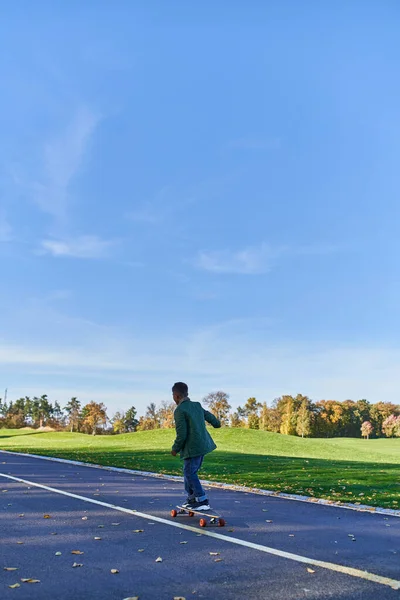 Menino bonito em outerwear montando penny board, asfalto, parque, época de outono, criança em roupas outonais — Fotografia de Stock