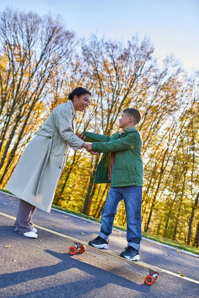 Happy childhood, african american mother and son on penny board, woman and boy, hold hands, autumn — Stock Photo