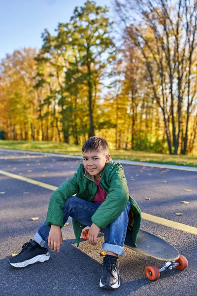 Bonito afro-americano menino sentado no penny board, parque de outono, temporada de outono, roupas quentes, outerwear — Fotografia de Stock