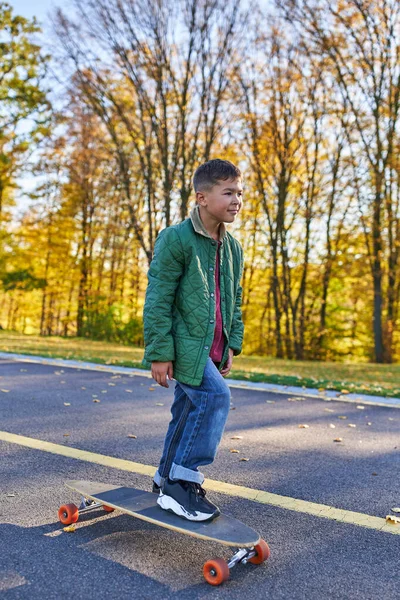 Preteen afro-americano menino em outerwear e jeans equitação penny board, outono parque, outono temporada — Fotografia de Stock