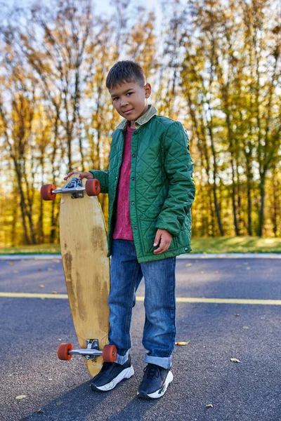 Comprimento total, bonito menino americano africano em outerwear segurando penny board, parque de outono, temporada de outono — Fotografia de Stock