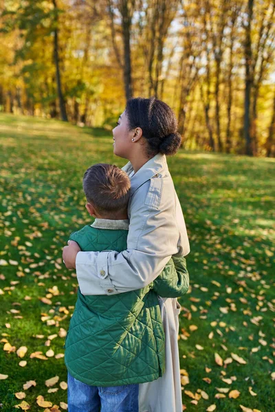 Amore materno, vista posteriore, donna afro-americana che abbraccia carino figlio, in piedi vicino a foglie d'oro — Foto stock