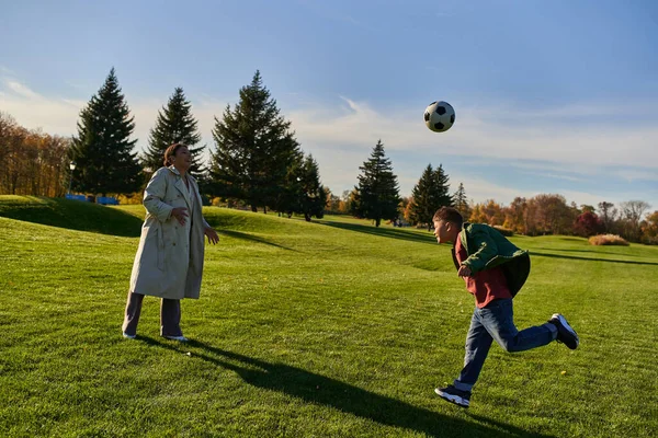 Head kick ball, african american boy playing football with happy mother, green field, soccer, fall — Stock Photo