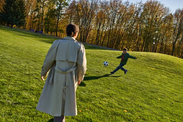 Lindo chico afroamericano jugando fútbol cerca de la madre en el campo verde, fútbol, otoño, temporada de otoño - foto de stock