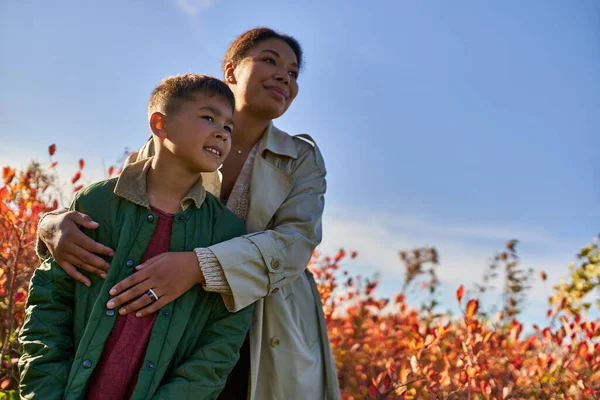 Happy african american mother in autumnal clothes embracing son, fall season, golden leaves — Stock Photo