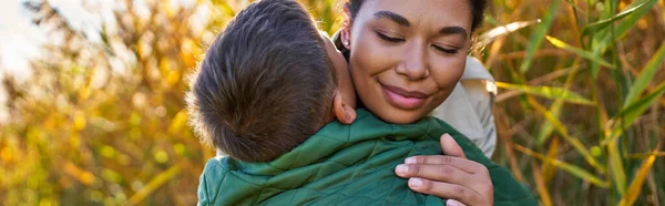Щастя, материнське кохання, афроамериканська мати обіймає сина в автономному верхньому одязі, банер — стокове фото
