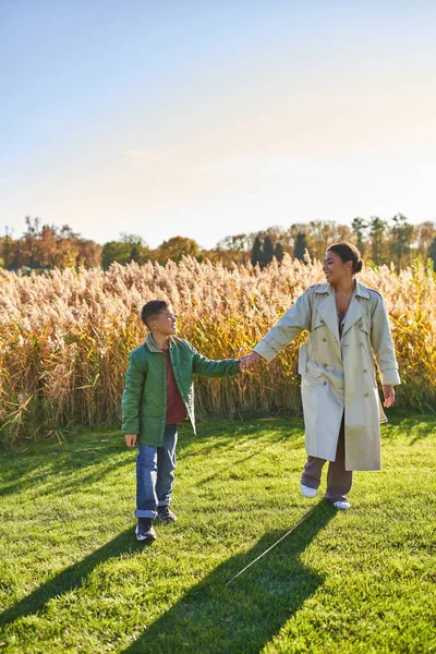 Madre e hijo que se unen, tomados de la mano, caminando en el campo, juntos, concepto de amor maternal, otoño - foto de stock