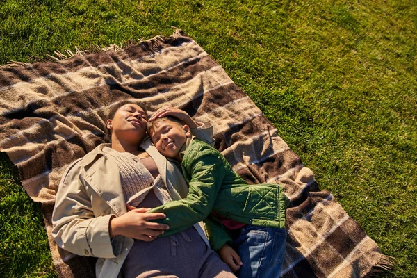 Vista superior, felicidad, amor maternal, mujer afroamericana y su hijo acostado sobre una manta, otoño, hierba - foto de stock