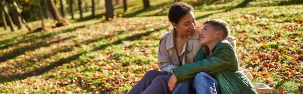 Материнська любов, весела афроамериканка і син сидить на траві з золотим листям, банер — стокове фото