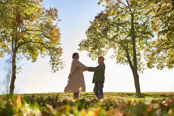Silhouette de femme et garçon tenant la main dans le parc d'automne, automne, liaison entre mère et fils — Photo de stock
