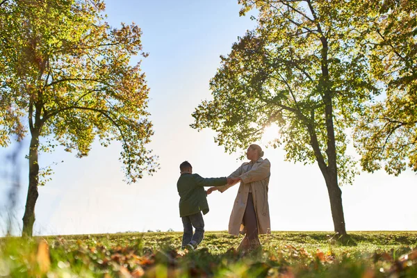 Silhouette of mother and child holding hands in autumn park, fall season, having fun, freedom, dance — Stock Photo