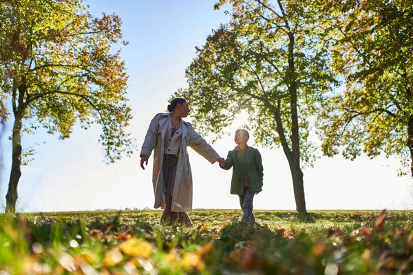 African american mother and child holding hands in autumn park, fall season, having fun, together — Stock Photo