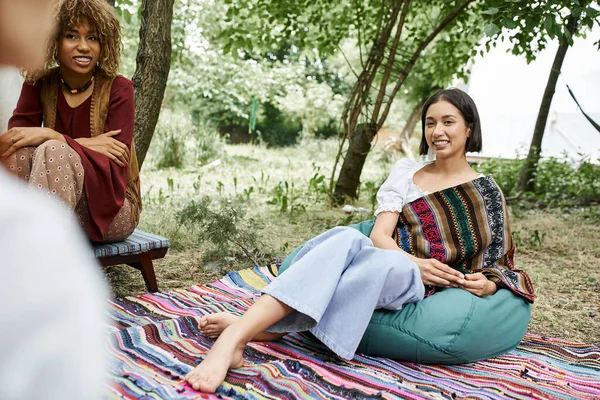 Positive interracial girlfriend in boho styled outfits talking outdoors in retreat center — Stock Photo