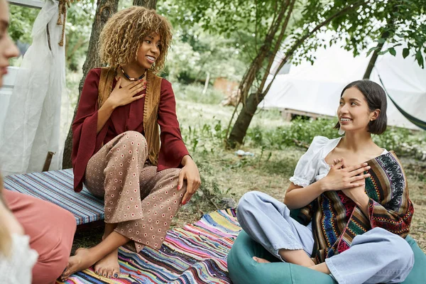 Smiling multiethnic women in boho outfits meditating on meadow outdoors in retreat center — Stock Photo