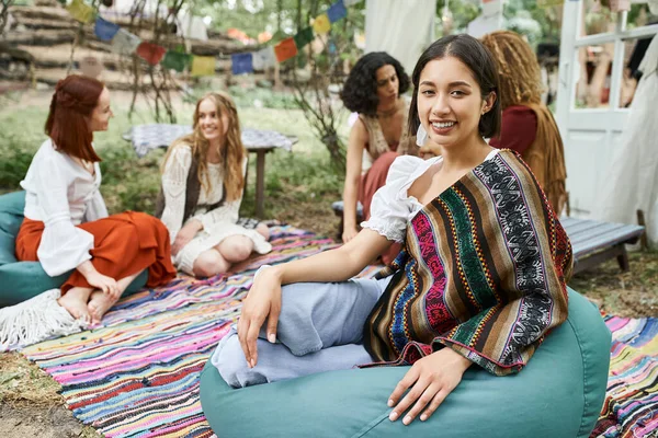 Smiling young woman in boho outfit looking at camera near multiethnic friends in retreat center — Stock Photo