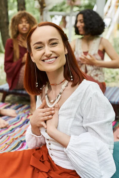 Portrait of cheerful woman sitting near blurred interracial friends outdoors in retreat center — Stock Photo