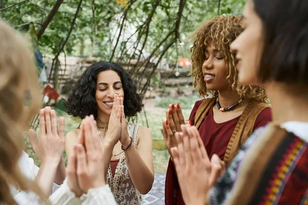 Smiling and stylish interracial women praying together outdoors in retreat center — Stock Photo