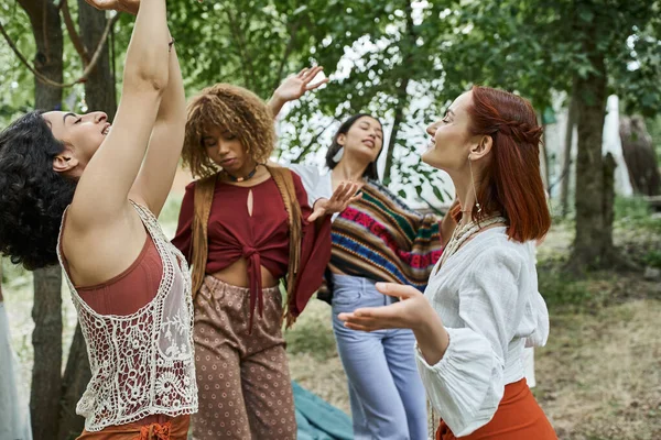 Positive interracial women in boho outfits dancing together outdoors in retreat center — Stock Photo