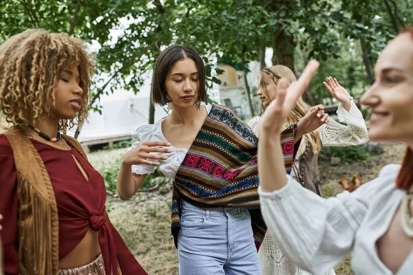 Young woman in boho outfit dancing near interracial friends outdoors in retreat center — Stock Photo