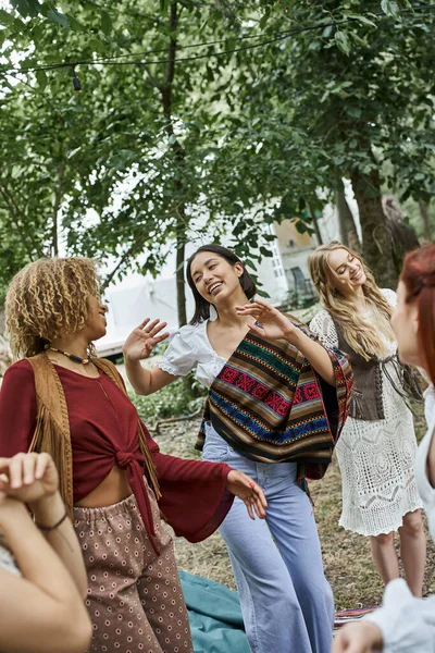 Joyful multiethnic women in boho outfits dancing together outdoors in retreat center — Stock Photo
