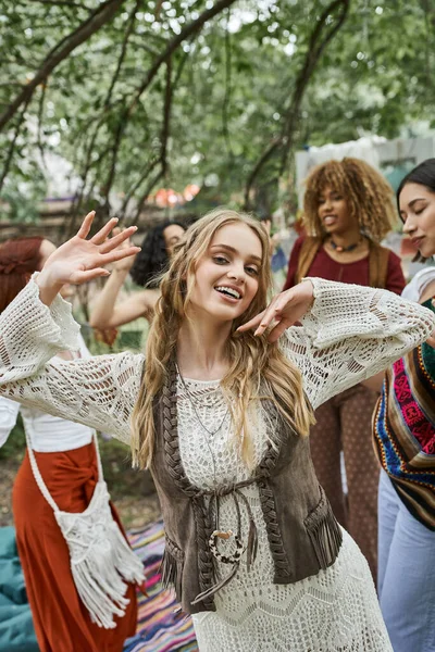 Joyful and trendy young woman dancing near interracial friends outdoors in retreat center — Stock Photo