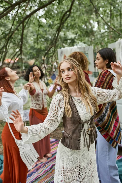 Young blonde woman in boho outfit dancing near interracial friends in retreat center — Stock Photo